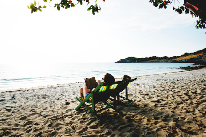 Retired person relaxing on a deckchair, reading a book on a beach paradise