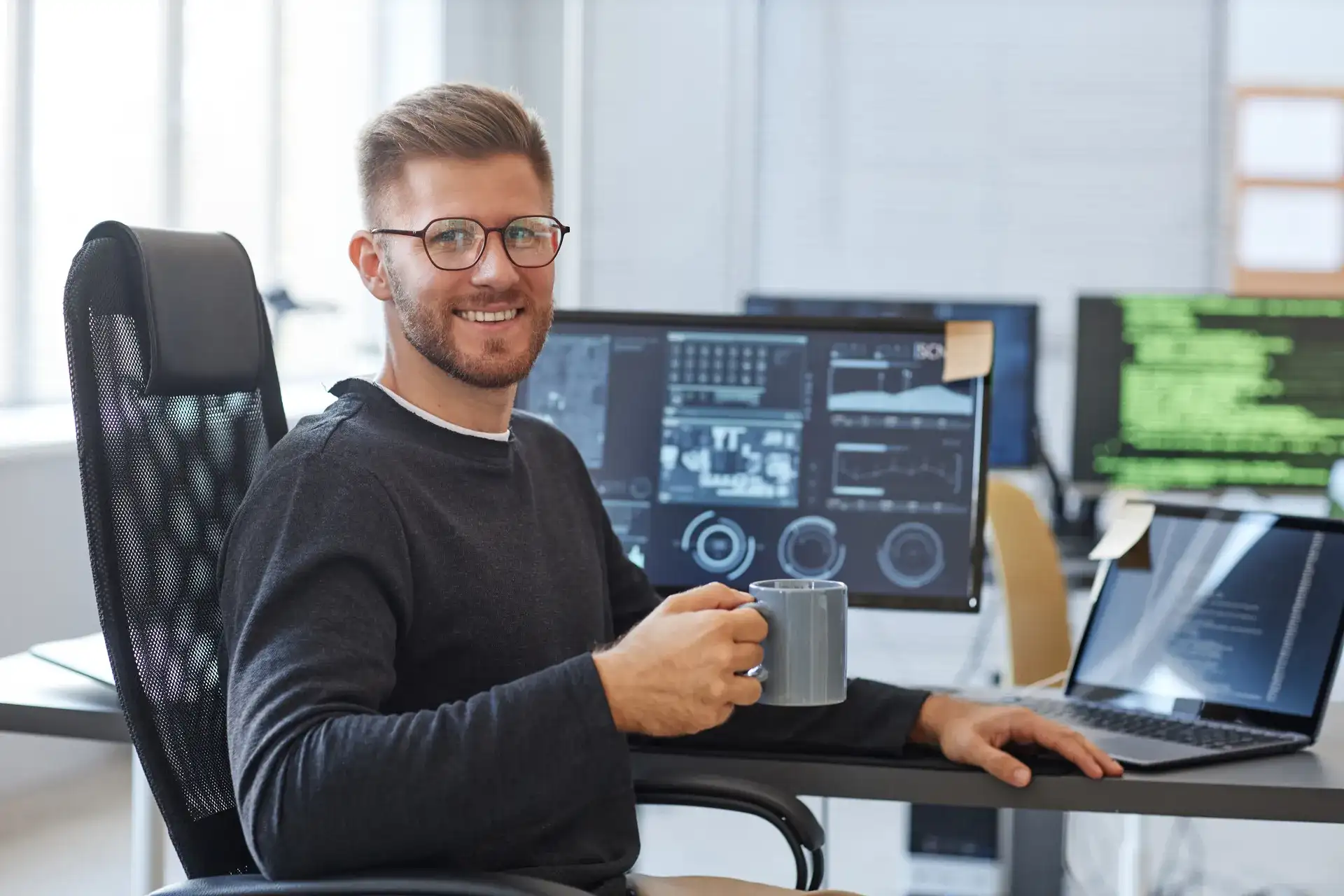 Office worker holding a mug in front of a computer showing technical information
